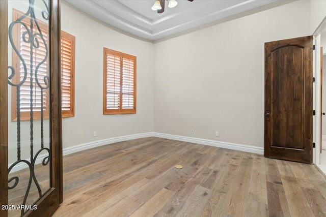 unfurnished room featuring ceiling fan, light wood-type flooring, and a tray ceiling