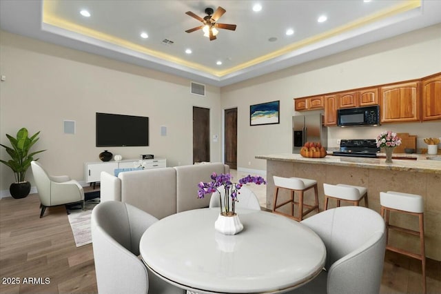 dining space with hardwood / wood-style floors, a raised ceiling, and ceiling fan