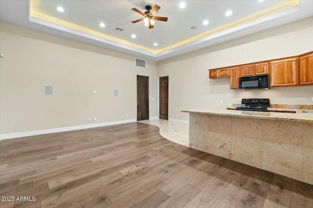 kitchen with hardwood / wood-style flooring, ceiling fan, light stone counters, black appliances, and a raised ceiling