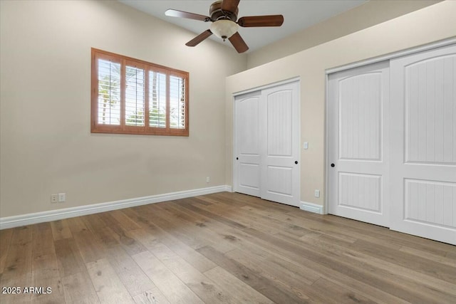 unfurnished bedroom with two closets, ceiling fan, and light wood-type flooring