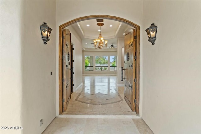 corridor featuring a raised ceiling and a chandelier