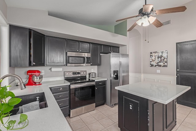 kitchen with lofted ceiling, sink, light tile patterned floors, stainless steel appliances, and a kitchen island