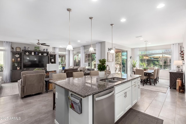 kitchen with white cabinetry, sink, stainless steel dishwasher, dark stone countertops, and a kitchen island with sink