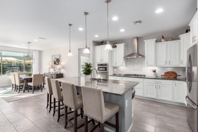 kitchen with decorative light fixtures, white cabinetry, wall chimney range hood, and appliances with stainless steel finishes