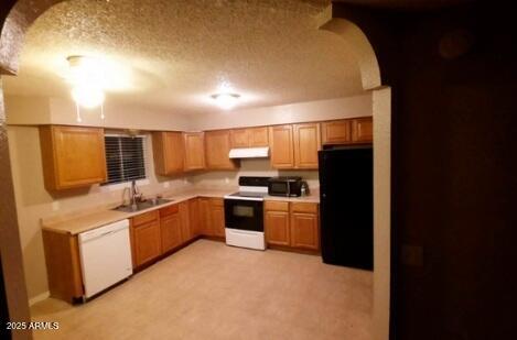 kitchen with under cabinet range hood, white appliances, a sink, arched walkways, and light countertops