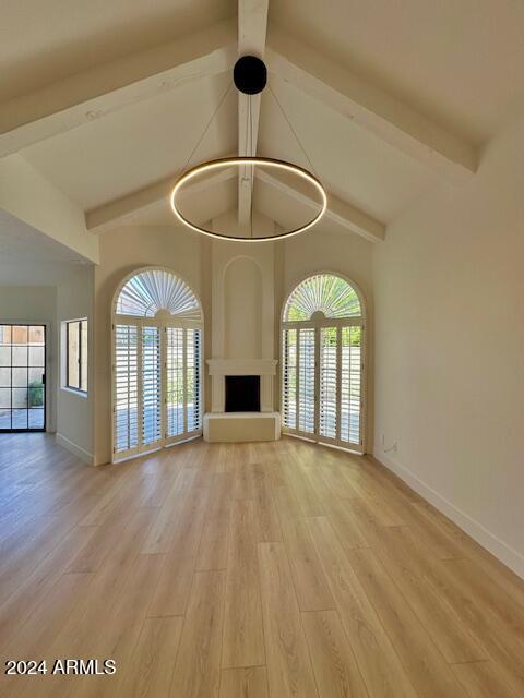 unfurnished living room featuring vaulted ceiling with beams, plenty of natural light, and light hardwood / wood-style floors