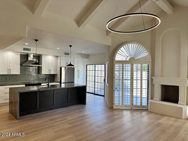 kitchen with white cabinets, wall chimney exhaust hood, decorative light fixtures, and light hardwood / wood-style flooring