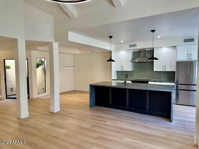 kitchen featuring stainless steel refrigerator, light hardwood / wood-style flooring, white cabinets, and wall chimney range hood