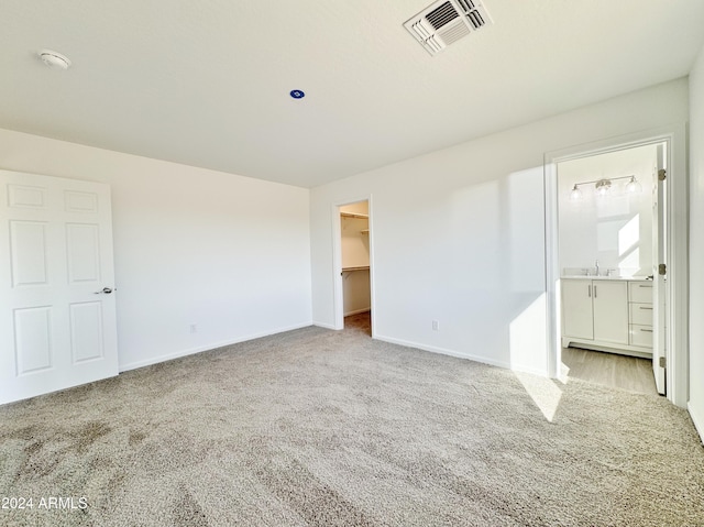 unfurnished bedroom with ensuite bathroom, a walk in closet, sink, light colored carpet, and a closet