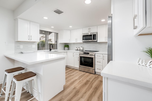 kitchen featuring white cabinets, kitchen peninsula, appliances with stainless steel finishes, and a kitchen breakfast bar