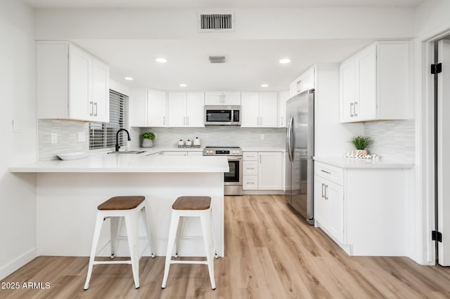 kitchen with a kitchen breakfast bar, white cabinets, sink, kitchen peninsula, and stainless steel appliances