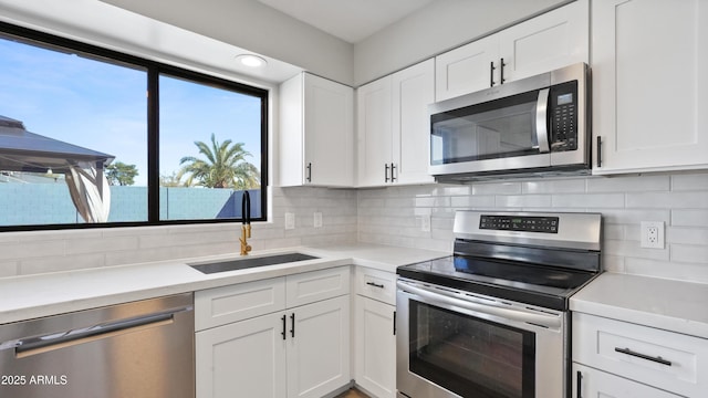 kitchen featuring appliances with stainless steel finishes, a sink, white cabinetry, and tasteful backsplash