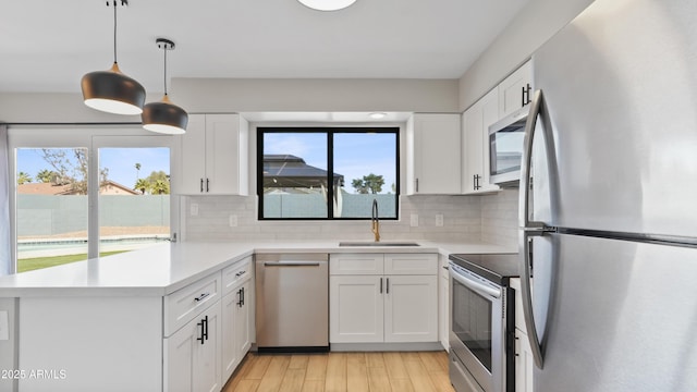 kitchen featuring stainless steel appliances, a peninsula, a sink, and white cabinets