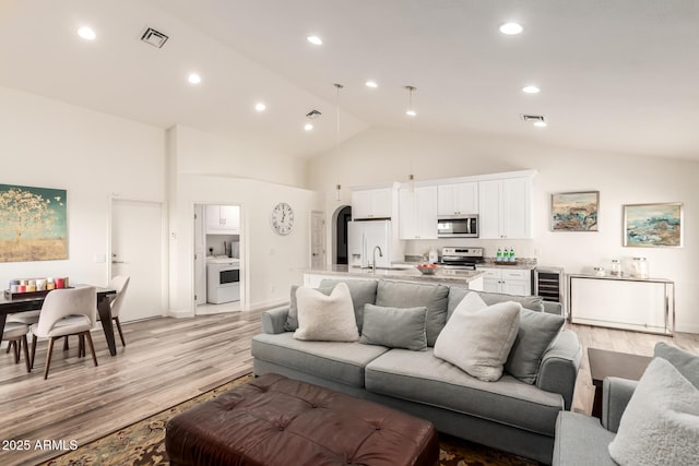 living room featuring high vaulted ceiling, beverage cooler, washer / clothes dryer, and light hardwood / wood-style flooring