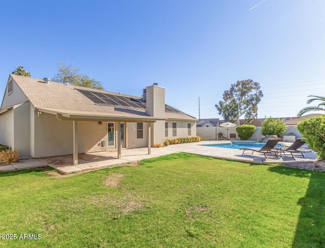 back of property with a fenced in pool, a patio area, a lawn, and solar panels