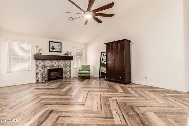 unfurnished room with a tile fireplace, ceiling fan, light parquet flooring, and high vaulted ceiling