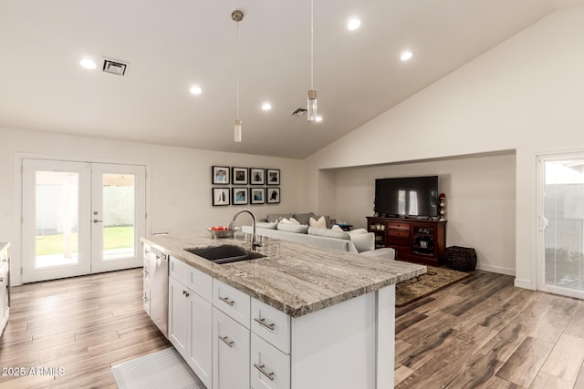 kitchen featuring light stone countertops, sink, decorative light fixtures, a kitchen island with sink, and white cabinets