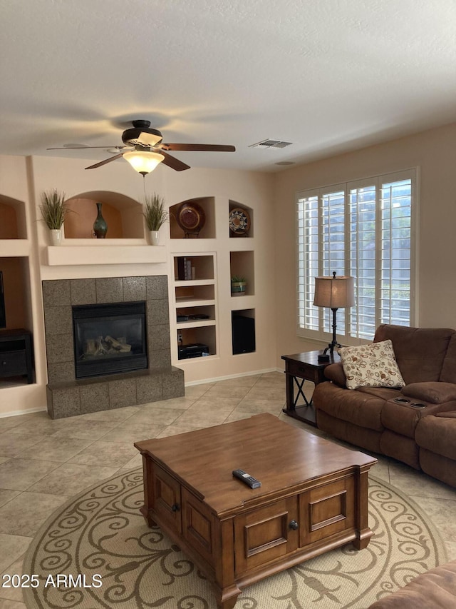 living room featuring built in shelves, light tile patterned flooring, a textured ceiling, a tile fireplace, and ceiling fan