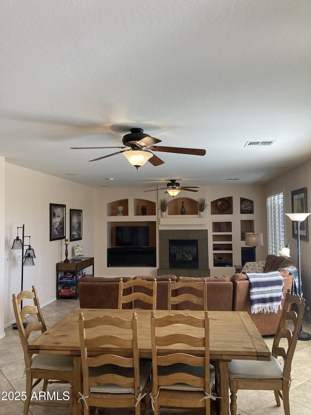 tiled dining space featuring ceiling fan and a fireplace