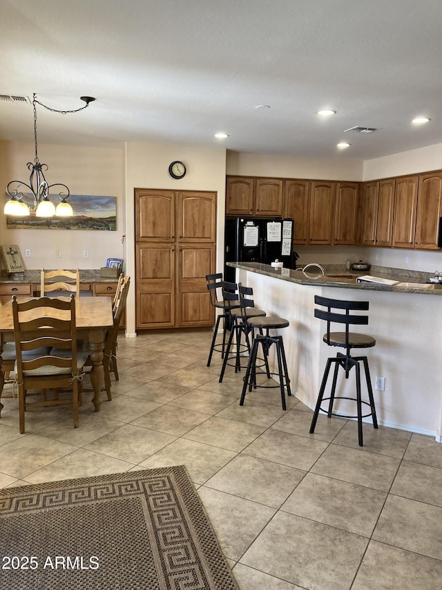 kitchen with an inviting chandelier, black fridge, decorative light fixtures, light tile patterned floors, and a kitchen breakfast bar