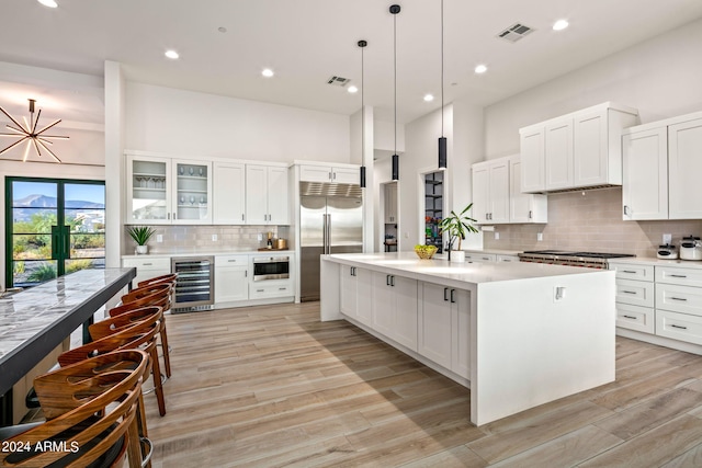 kitchen featuring pendant lighting, a kitchen island, beverage cooler, appliances with stainless steel finishes, and light hardwood / wood-style floors