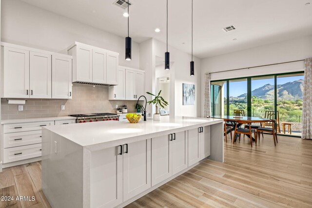 kitchen featuring pendant lighting, an island with sink, a mountain view, and white cabinetry