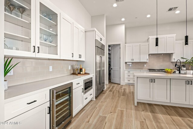 kitchen featuring beverage cooler, stainless steel appliances, hanging light fixtures, and white cabinetry