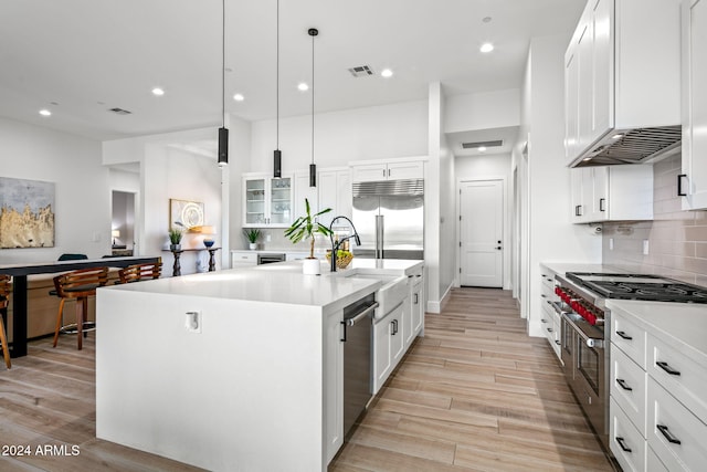 kitchen with an island with sink, white cabinets, decorative light fixtures, and high quality appliances