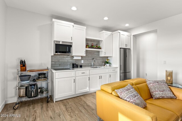 kitchen featuring stainless steel appliances, light hardwood / wood-style floors, white cabinets, and tasteful backsplash