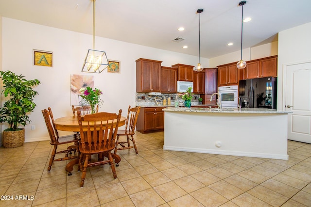 kitchen with light tile patterned floors, white appliances, a kitchen island with sink, backsplash, and decorative light fixtures