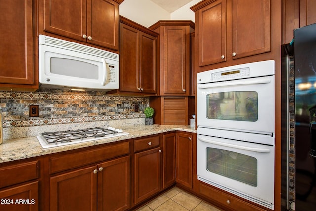 kitchen featuring light stone counters, white appliances, tasteful backsplash, and light tile patterned floors