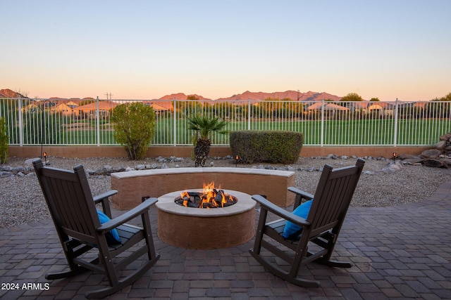 patio terrace at dusk with a mountain view, a fire pit, and a lawn