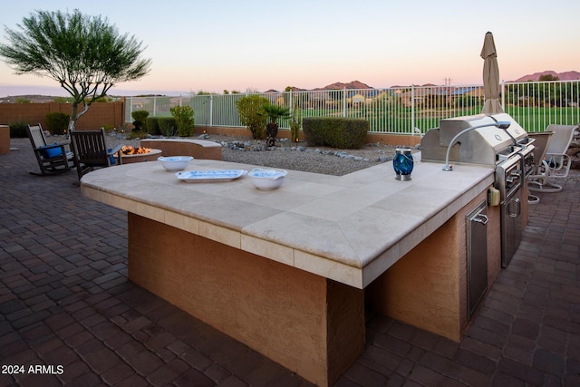 patio terrace at dusk featuring exterior kitchen and an outdoor fire pit