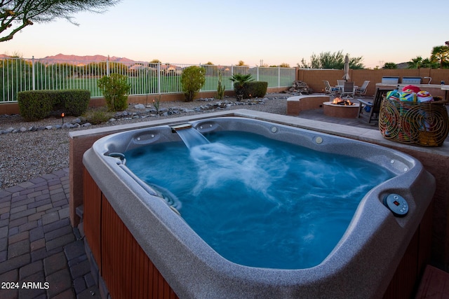 pool at dusk with a hot tub, a patio, and an outdoor fire pit