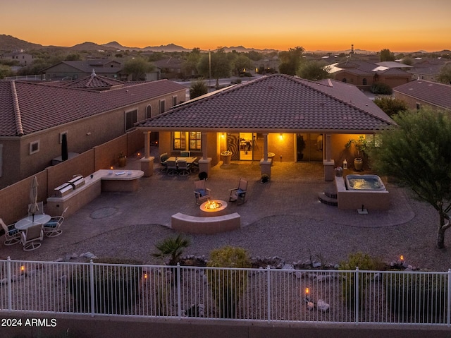 back house at dusk with exterior kitchen, a mountain view, a patio area, and an outdoor fire pit