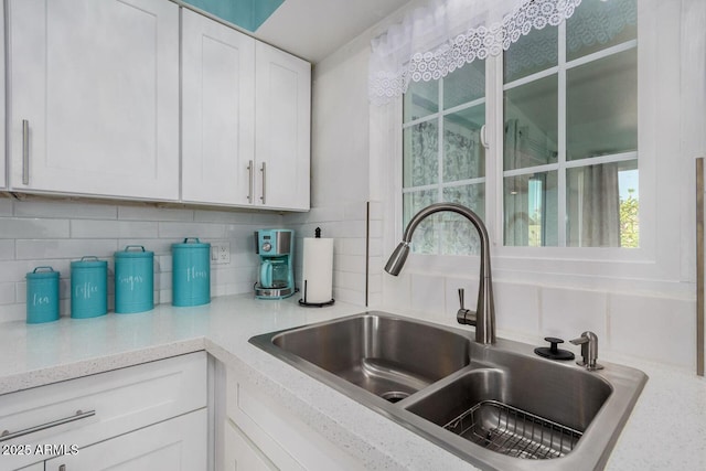 kitchen featuring white cabinetry, sink, light stone countertops, and tasteful backsplash