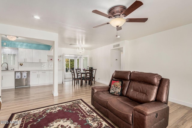 living room with ceiling fan with notable chandelier, sink, and light hardwood / wood-style floors