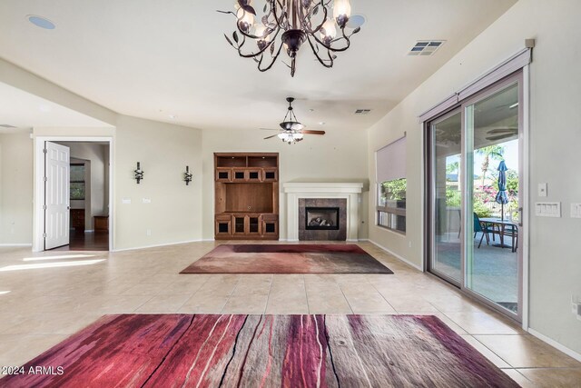 unfurnished living room with light tile patterned floors, a tiled fireplace, and ceiling fan with notable chandelier