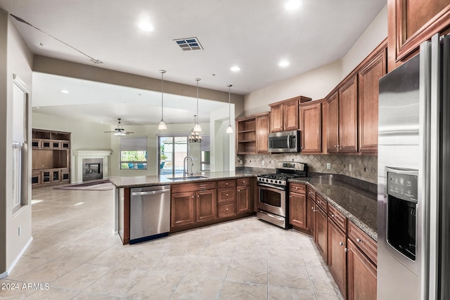 kitchen featuring pendant lighting, ceiling fan with notable chandelier, kitchen peninsula, sink, and appliances with stainless steel finishes