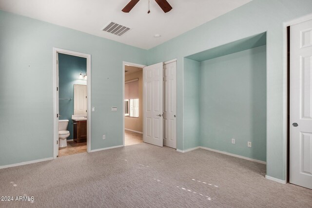 unfurnished bedroom with light colored carpet, ensuite bathroom, and ceiling fan