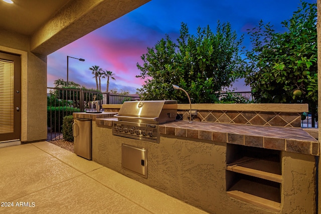 patio terrace at dusk with a grill and an outdoor kitchen