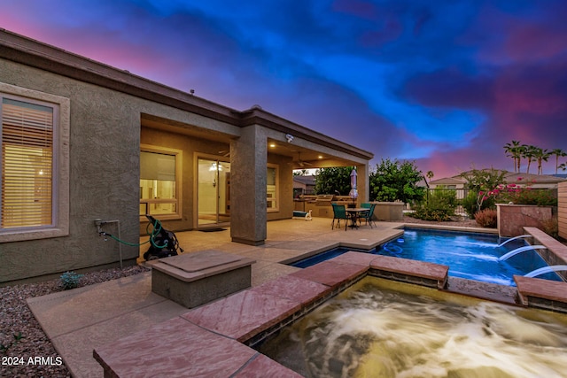 pool at dusk with an in ground hot tub, pool water feature, and a patio