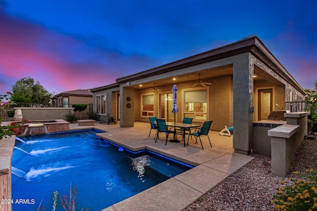 pool at dusk featuring pool water feature and a patio