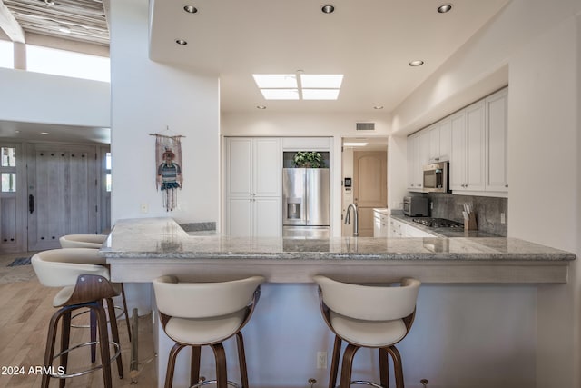 kitchen with white cabinets, a skylight, kitchen peninsula, stainless steel appliances, and light hardwood / wood-style floors