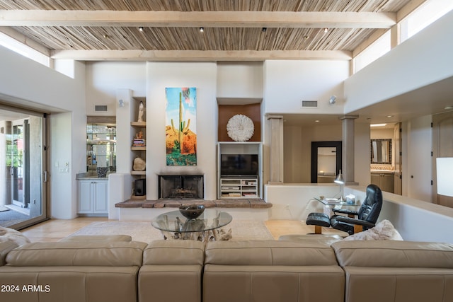 living room featuring a towering ceiling, ornate columns, beamed ceiling, and built in features