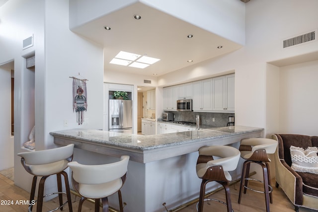 kitchen featuring kitchen peninsula, tasteful backsplash, white cabinetry, appliances with stainless steel finishes, and light stone countertops