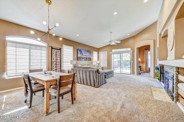 carpeted dining room featuring a stone fireplace, vaulted ceiling, and ceiling fan with notable chandelier