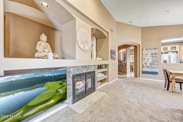 living room featuring vaulted ceiling, a stone fireplace, carpet floors, and built in shelves