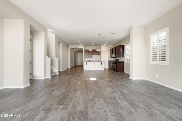 20473 W Legend Trl, Buckeye, AZ 85396 - unfurnished living room with arched walkways, a chandelier, wood finished floors, baseboards, and recessed lighting
