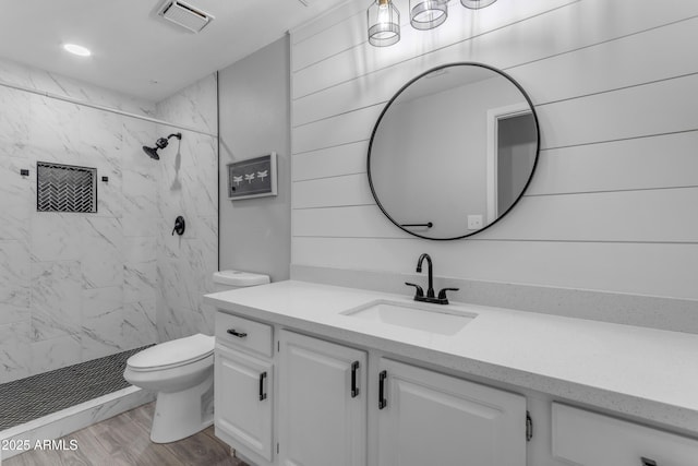 bathroom featuring hardwood / wood-style flooring, vanity, toilet, and tiled shower